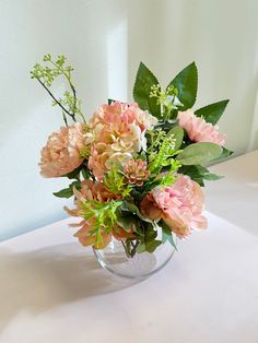 a vase filled with lots of pink flowers on top of a white tablecloth covered table