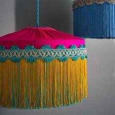 two colorful lamps hanging from the ceiling with fringes on each lamp shade, one pink and one blue