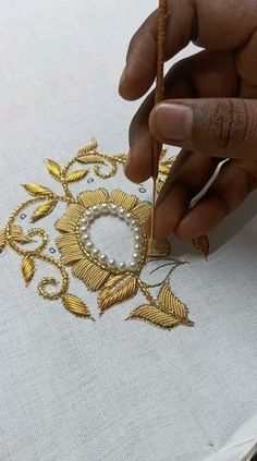 a person is working on an embroidered piece with gold thread and pearls in the middle