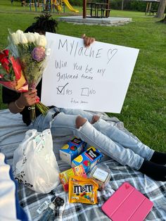 a woman sitting on top of a blanket holding a bouquet of flowers next to a sign