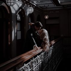 a man and woman standing on top of a balcony next to an iron railing in the dark