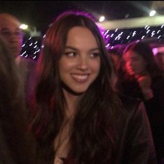 a woman is smiling at the camera in front of some people and purple lights,