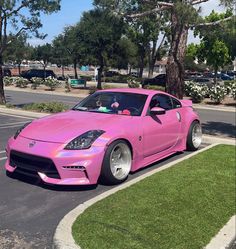 a pink sports car is parked on the side of the road in front of some trees