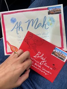 a person holding a red envelope with writing on it and a postcard attached to the envelope