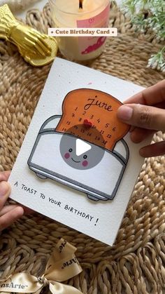 someone holding up a birthday card with a toaster on it and candles in the background