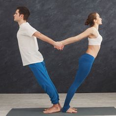 a man and woman holding hands while standing on a yoga mat in front of a wall