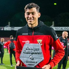 a man holding a plaque on top of a soccer field at night with other people in the background