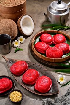 some red cookies are sitting on a wooden plate next to two bowls with flowers and coconuts