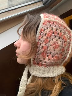 a woman wearing a crocheted hat looking out the window