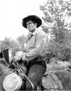 a black and white photo of a man on a horse wearing a cowboy hat, holding a lasso