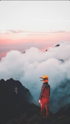 a person standing on top of a mountain with clouds in the sky behind them,