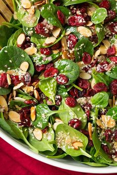 spinach salad with cranberries and almonds in a white bowl on a red cloth