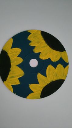 a painted disc with sunflowers on it sitting on a white table next to a wall