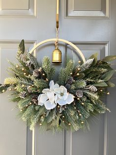 a wreath with white flowers and greenery hangs on the front door, next to a golden bell