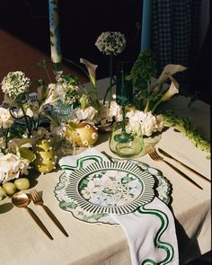 a table topped with flowers and candles on top of a white table cloth next to utensils