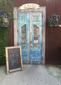 an old blue door is next to a chalkboard sign that says tacos just for you