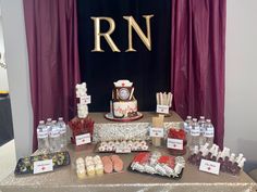 a table topped with lots of desserts and candies next to a purple curtain