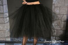 a woman wearing a black tulle skirt and crop top standing in front of a fireplace