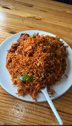 a white plate topped with rice and meat on top of a wooden table next to a fork