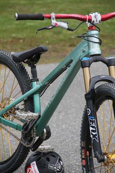 a green mountain bike parked on the side of a road next to a helmet and glove