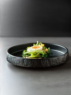 a black plate topped with an egg and broccoli