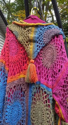 a colorful crocheted shawl is hanging on a clothes rack outside with trees in the background