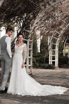 a bride and groom standing under an arbor in their wedding dress, posing for the camera