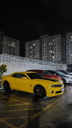 several cars are parked in a parking lot with tall buildings in the background at night