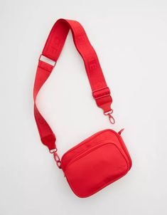 a small red bag on a white surface with a strap around the neck and shoulder