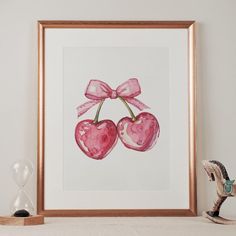 two cherries with pink bows are displayed in front of a wooden frame on a shelf