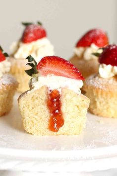 small cupcakes with strawberries and whipped cream on top are sitting on a white plate