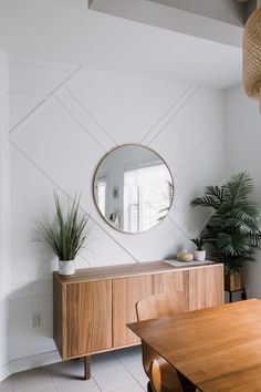 a dining room with a table, mirror and potted plants on the sideboard