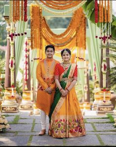 two people standing in front of an archway with flowers and garlands on the ground