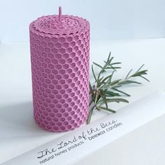 a pink candle sitting on top of a white table next to a plant and paper