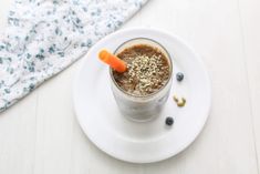 a smoothie is sitting on a white plate with a carrot sticking out of it