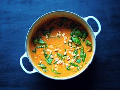 a pot filled with soup and vegetables on top of a blue tablecloth next to a spoon