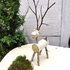 a small metal deer statue sitting on top of a white table next to a tree