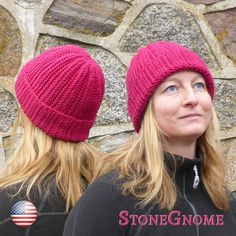 two women wearing knitted hats standing in front of a stone wall with an american flag pin on it