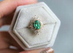 a person holding an emerald and diamond ring