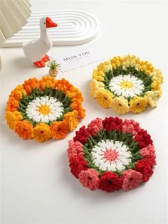 three crocheted flower coasters sitting on top of a white table next to a duck