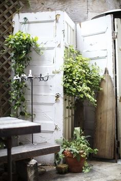 an open door with plants growing out of it next to a bench and table in the corner