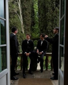 three men in tuxedos are sitting on a bench and talking to each other