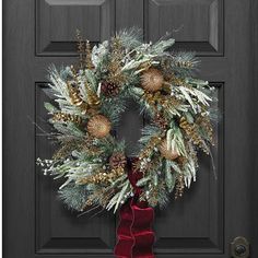 a wreath with pine cones and evergreens hanging on a front door, next to a red bow