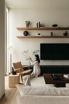 a woman is sitting on the floor in her living room and looking at the television