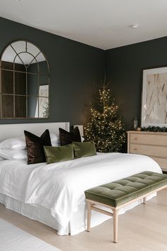 a bedroom decorated for christmas with a bed, mirror and tree in the corner on the wall