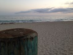 a wooden post sitting on top of a sandy beach next to the ocean at sunset