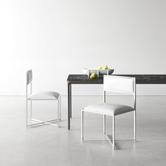 two white chairs and a table with fruit on it in front of a white wall