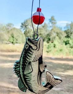 a metal fish hanging from a hook on a string with a red ball in the background