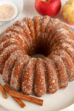 a bundt cake on a white plate with cinnamon sticks and apples in the background