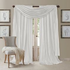 a living room with a chair and white drapes on the windowsill, in front of some framed pictures